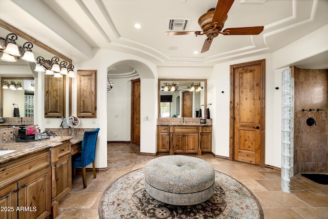 bathroom with ceiling fan, vanity, a tray ceiling, and a tile shower