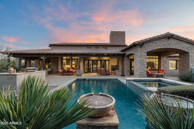 pool at dusk featuring a patio area, area for grilling, an outdoor bar, an in ground hot tub, and an outdoor living space