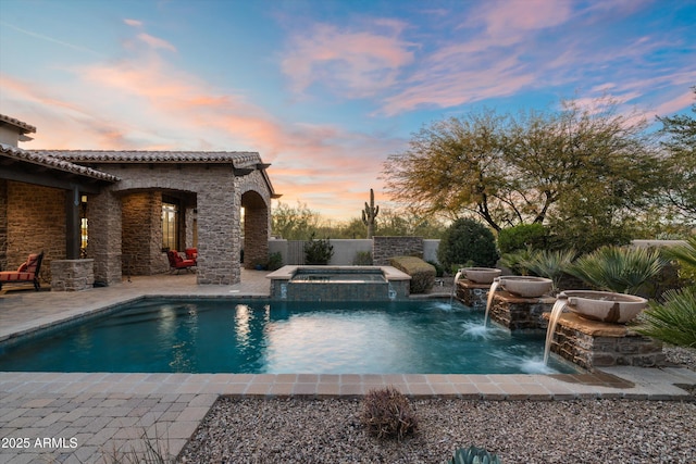 pool at dusk featuring an in ground hot tub, pool water feature, and a patio area