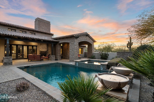 pool at dusk with an outdoor living space, a patio, and an in ground hot tub