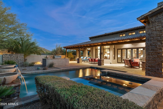 pool at dusk with pool water feature, a jacuzzi, a patio area, area for grilling, and an outdoor hangout area