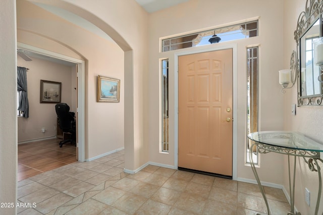 foyer with arched walkways, light tile patterned flooring, and baseboards