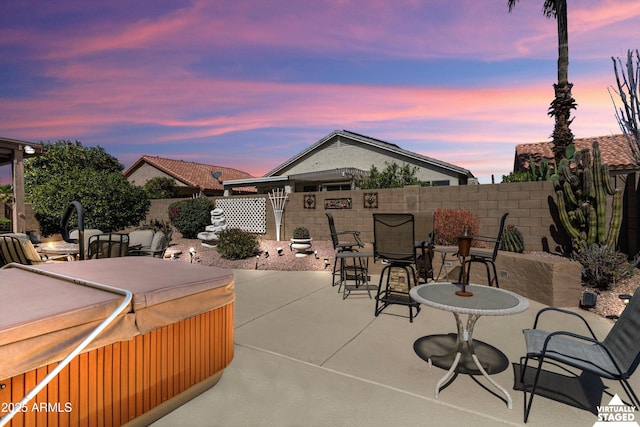 patio terrace at dusk featuring outdoor dining area, a fenced backyard, and a hot tub