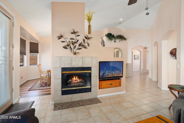 living room with lofted ceiling, a tiled fireplace, a ceiling fan, and tile patterned floors