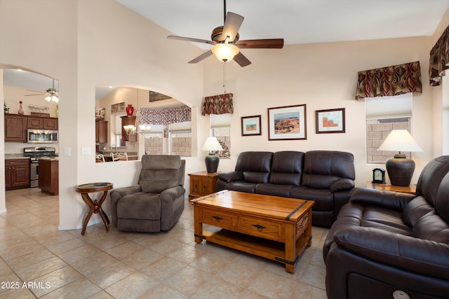 living room featuring arched walkways, ceiling fan with notable chandelier, a towering ceiling, and baseboards