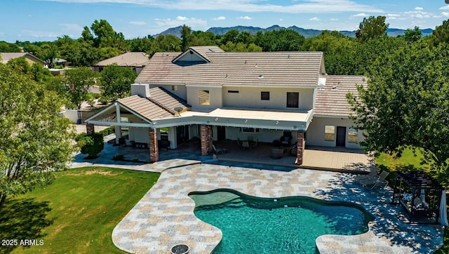 back of property with a patio area, stucco siding, a mountain view, and a yard