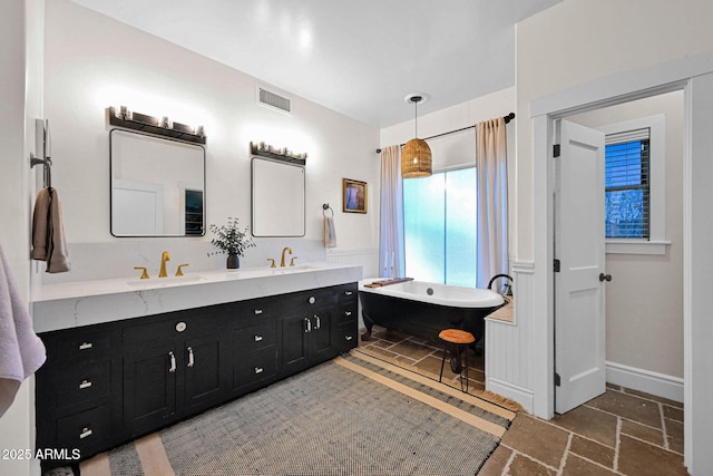 full bathroom featuring a sink, visible vents, stone tile floors, and a freestanding tub