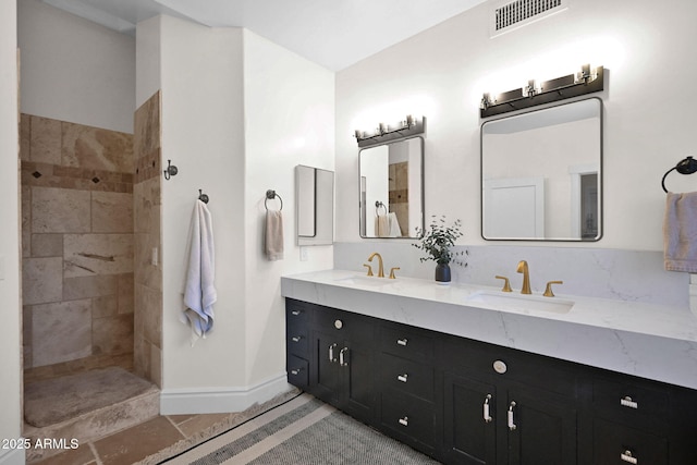 bathroom with double vanity, visible vents, a tile shower, and a sink