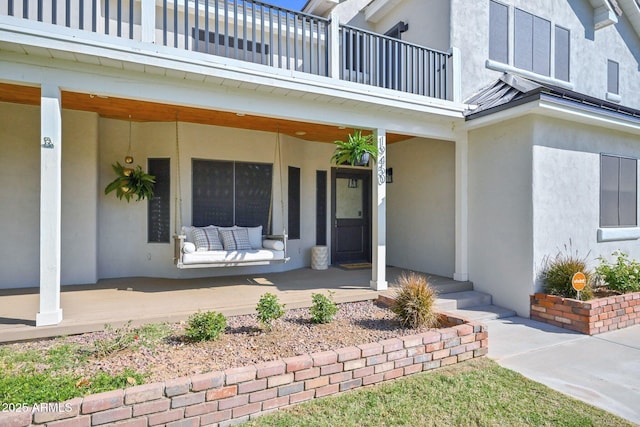 view of exterior entry with stucco siding, a balcony, and covered porch