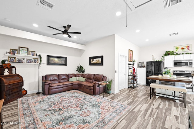 living room featuring light wood-type flooring, visible vents, attic access, and a ceiling fan