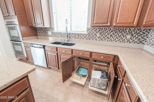 40232 W Marion May Ln, Maricopa, AZ 85138 - kitchen featuring appliances with stainless steel finishes, a sink, light tile patterned floors, backsplash, and brown cabinetry