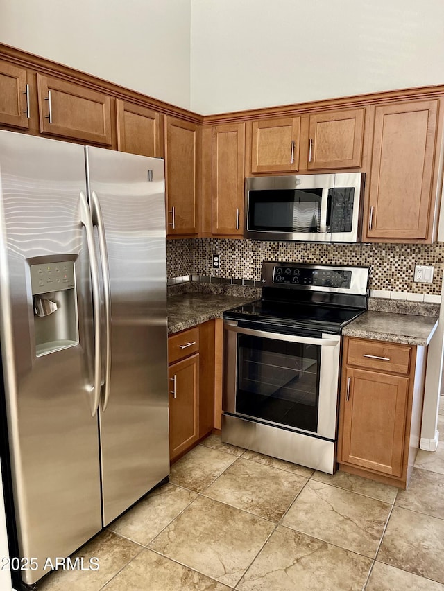 5749 S 247th Dr, Buckeye, AZ 85326 - kitchen with stainless steel appliances, dark countertops, decorative backsplash, and brown cabinetry