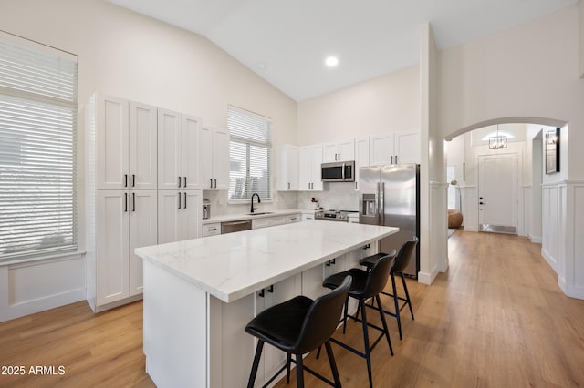 1748 E Cortez Dr, Gilbert, AZ 85234 - kitchen featuring a kitchen island, appliances with stainless steel finishes, arched walkways, light stone countertops, and a breakfast bar