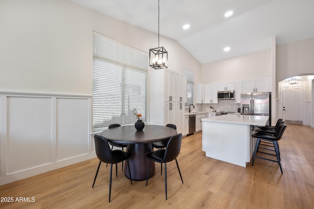 1748 E Cortez Dr, Gilbert, AZ 85234 - dining area featuring arched walkways, wainscoting, light wood-type flooring, high vaulted ceiling, and an inviting chandelier
