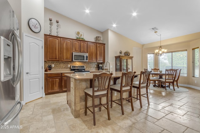 6870 S Justin Way, Chandler, AZ 85249 - kitchen featuring stainless steel appliances, stone tile flooring, tasteful backsplash, a chandelier, and a breakfast bar area