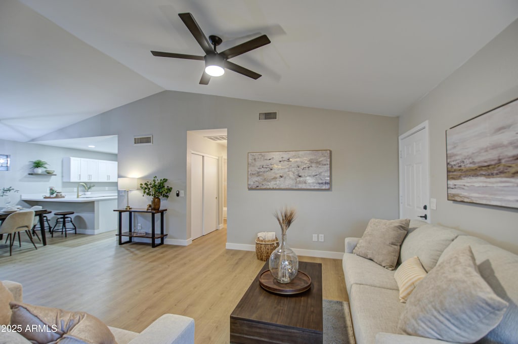 living room featuring ceiling fan, vaulted ceiling, and light wood-type flooring