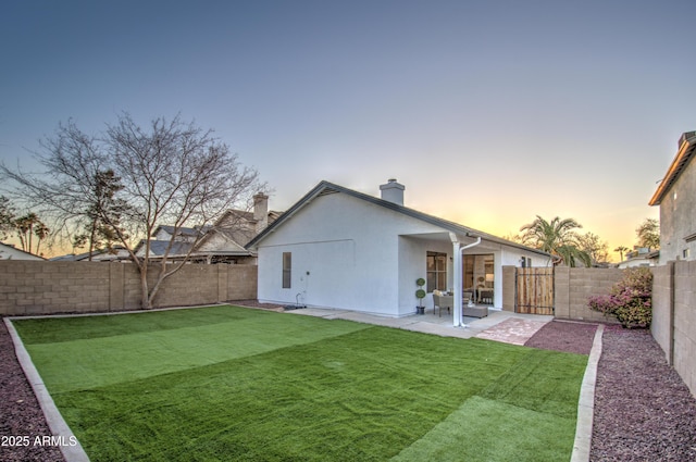 back house at dusk with a patio and a yard