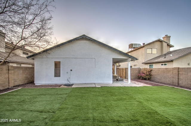 back house at dusk with a lawn, central air condition unit, and a patio area