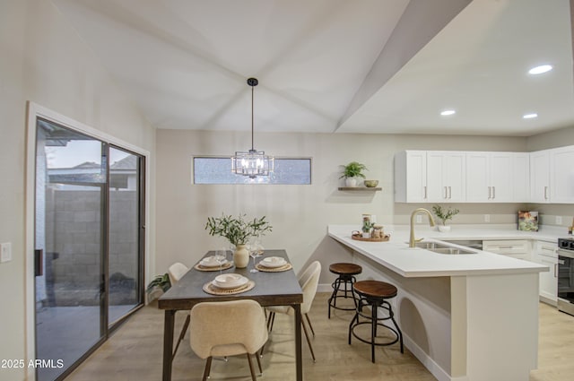 dining area with lofted ceiling, a chandelier, sink, and light hardwood / wood-style flooring