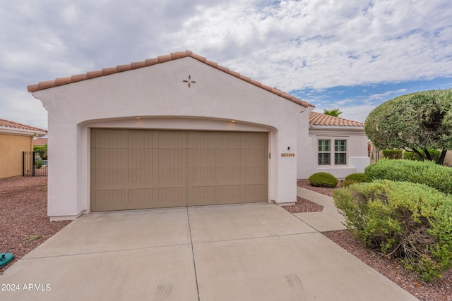 mediterranean / spanish house featuring concrete driveway, a tile roof, an attached garage, fence, and stucco siding