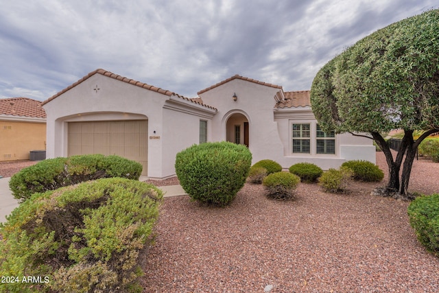 mediterranean / spanish house with an attached garage, a tiled roof, cooling unit, and stucco siding