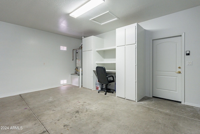 unfurnished office with attic access, water heater, unfinished concrete flooring, and baseboards