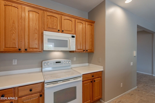 kitchen featuring brown cabinetry, white appliances, light countertops, and baseboards