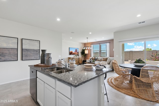 kitchen featuring visible vents, stainless steel dishwasher, a sink, dark stone countertops, and an island with sink