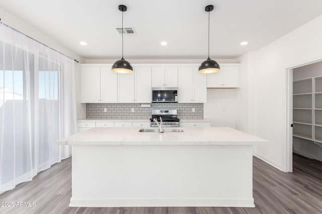 kitchen with appliances with stainless steel finishes, white cabinets, a center island with sink, and light stone counters