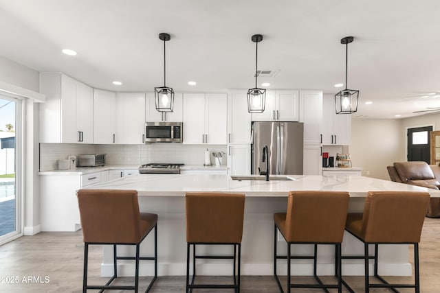 kitchen featuring stainless steel appliances, a sink, light countertops, light wood-type flooring, and decorative backsplash