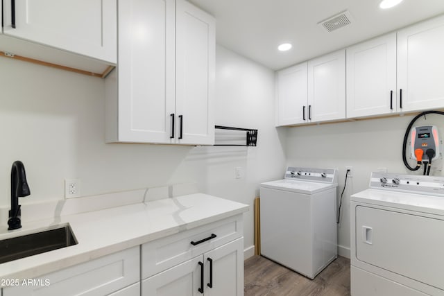 clothes washing area with cabinet space, light wood finished floors, visible vents, washer and clothes dryer, and a sink