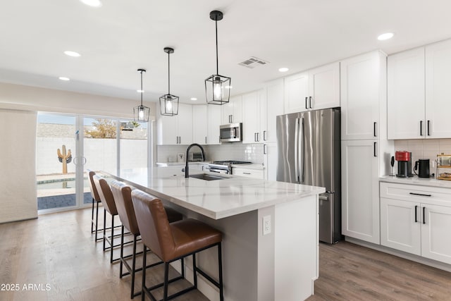 kitchen with visible vents, appliances with stainless steel finishes, wood finished floors, white cabinetry, and a sink