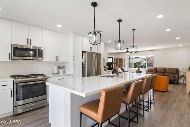 kitchen with decorative backsplash, open floor plan, wood finished floors, stainless steel appliances, and a sink