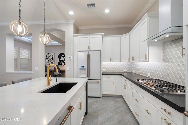 kitchen featuring visible vents, high end white refrigerator, a sink, stainless steel gas stovetop, and wall chimney range hood