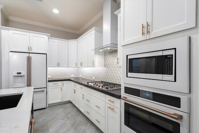 kitchen featuring ornamental molding, appliances with stainless steel finishes, white cabinets, wall chimney range hood, and decorative backsplash