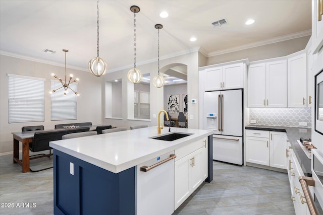 kitchen featuring a kitchen island with sink, high end white fridge, ornamental molding, decorative backsplash, and a sink