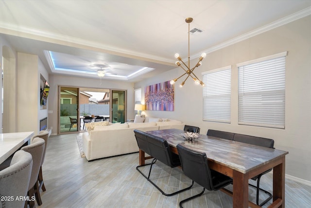 dining space featuring visible vents, crown molding, light wood-type flooring, a tray ceiling, and an inviting chandelier