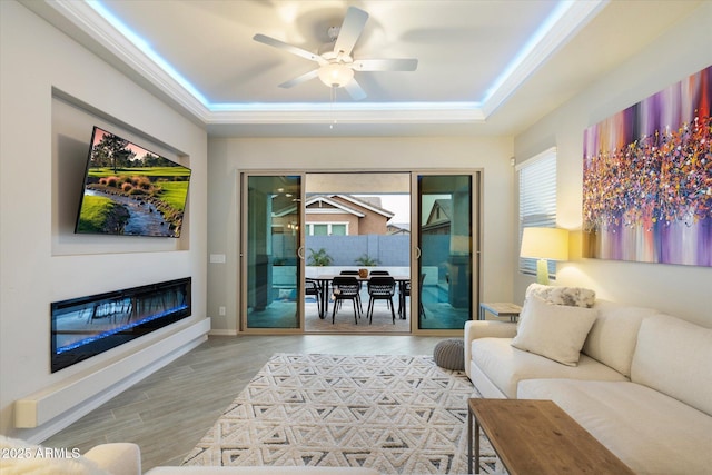 living room featuring a ceiling fan, a tray ceiling, and wood finished floors