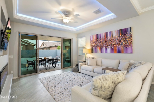 living room with visible vents, wood finished floors, crown molding, a raised ceiling, and ceiling fan