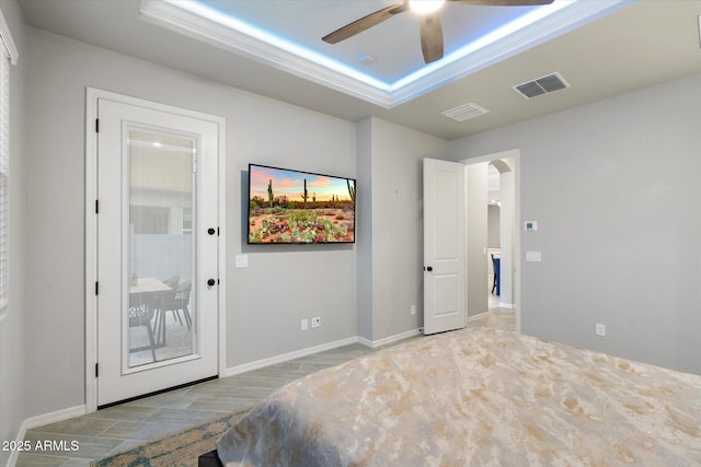 bedroom with visible vents, a ceiling fan, a tray ceiling, arched walkways, and baseboards