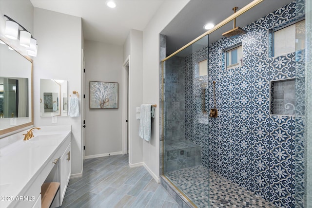 bathroom with vanity, baseboards, wood finish floors, recessed lighting, and a tile shower