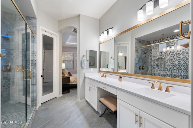 ensuite bathroom featuring a shower stall, wood finished floors, double vanity, and a sink