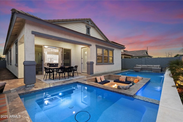 back of house at dusk with an outdoor living space with a fire pit, a patio area, fence, and stucco siding