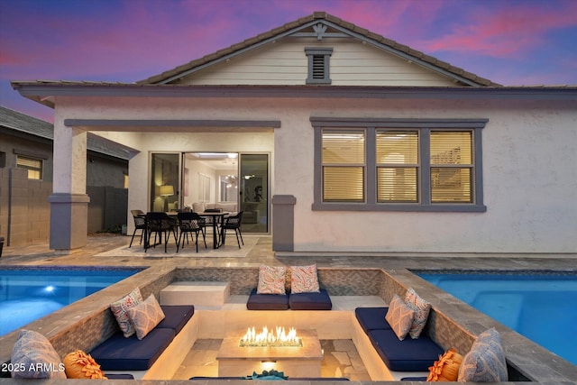 rear view of property featuring a patio area, stucco siding, a tiled roof, and an outdoor living space with a fire pit