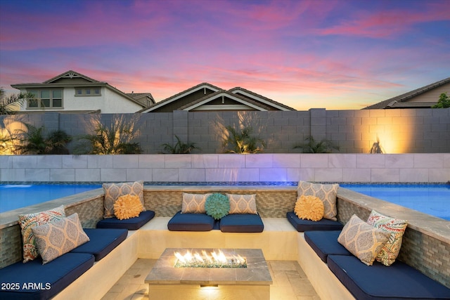 pool at dusk with an outdoor living space with a fire pit, a patio area, a fenced backyard, and a fenced in pool