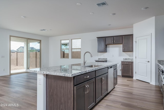 kitchen featuring a kitchen island with sink, light wood-style flooring, dark brown cabinetry, a sink, and visible vents