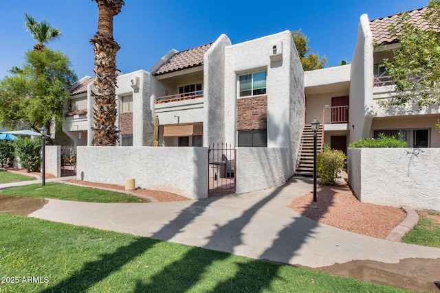 view of front facade with stucco siding, a tile roof, a gate, a fenced front yard, and stairway