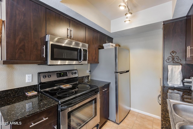 kitchen featuring dark brown cabinetry, stainless steel appliances, dark stone counters, and a sink