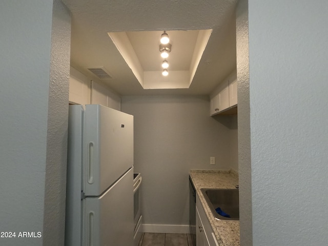 kitchen featuring a raised ceiling, stainless steel dishwasher, white refrigerator, white cabinetry, and sink