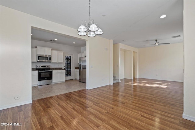 kitchen featuring light hardwood / wood-style floors, appliances with stainless steel finishes, pendant lighting, ceiling fan with notable chandelier, and white cabinets